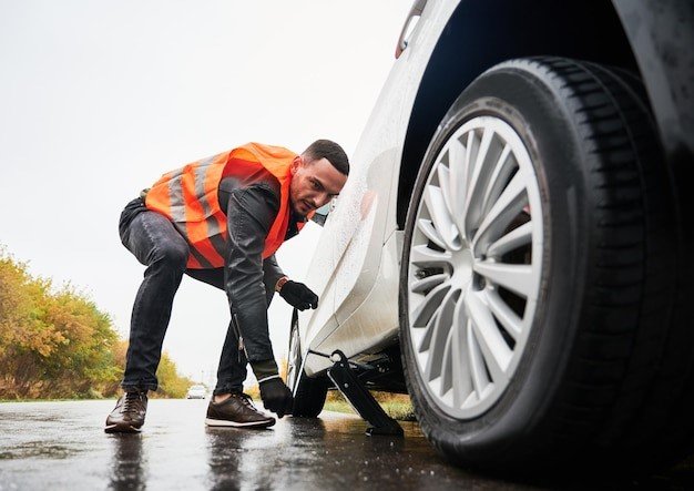 A man in an orange vest is changing the tire of his car.