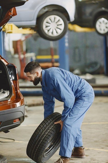 A man in blue work clothes is holding a tire.