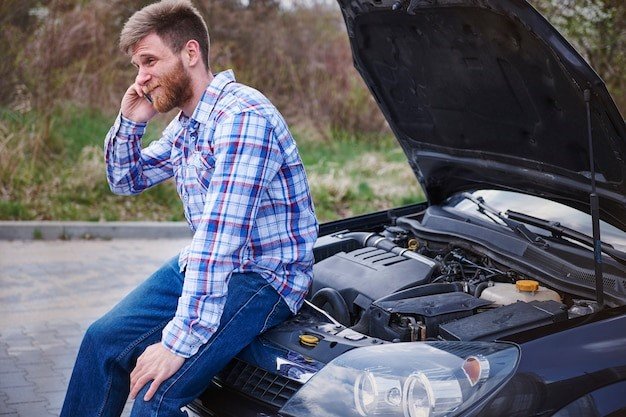 A man sitting on the hood of his car talking on a phone.